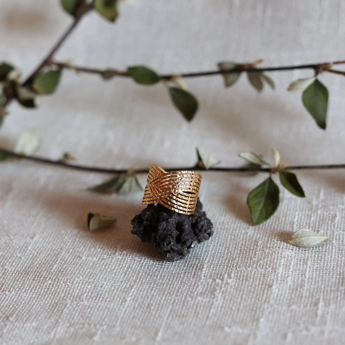 Bague Avenir ajustable, au design géométrique en acier inoxydable doré, posée sur une pierre volcanique, sur fond de toile beige et feuillage.