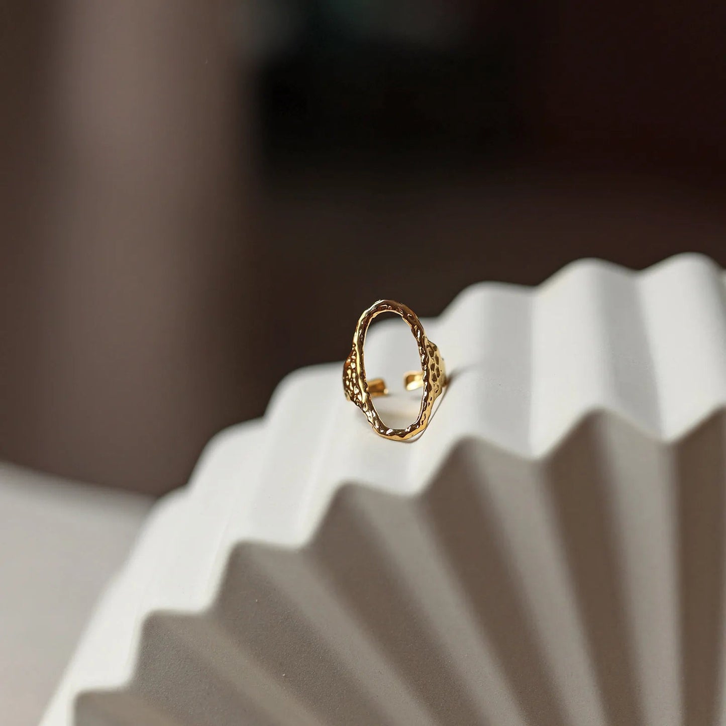 Bague Maintenant en acier inoxydable doré, ovale martelée et réglable, présentée sur un fond beige texturé.