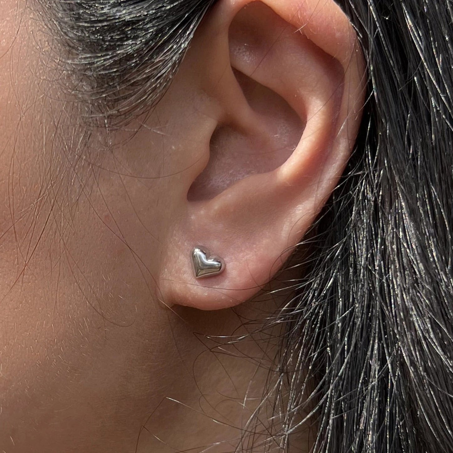 Boucles d'oreilles "Tendre discrétion" de Visée, en forme de cœur en acier argenté, portées à l'oreille.