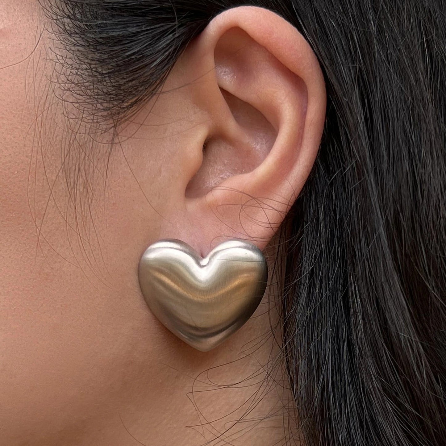 Boucles d'oreilles "S'aimer", en maxi cœurs argentés mat, en acier Inoxydable, portées à l'oreille.