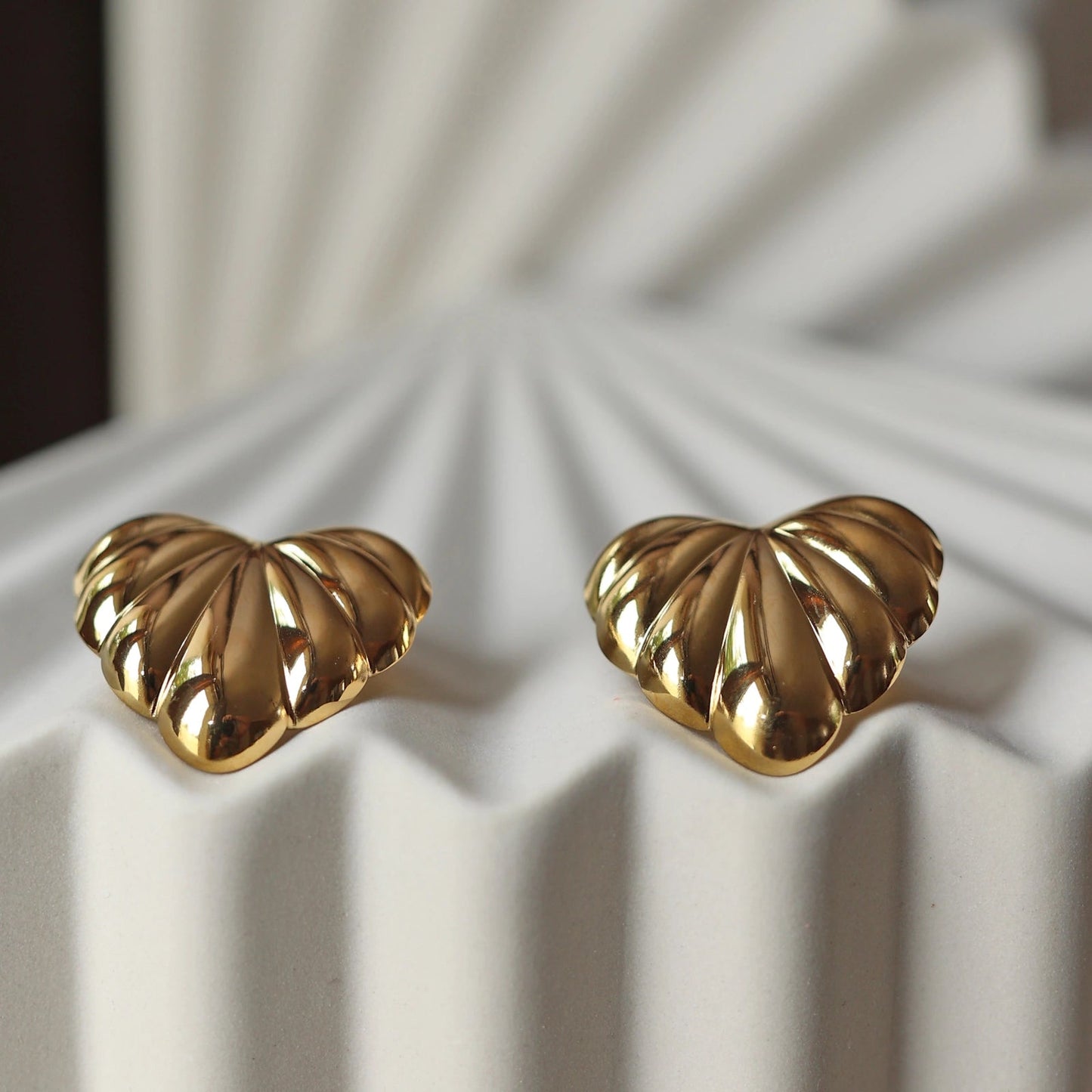 Boucles d'oreilles "Coeur audacieux", en acier inoxydable doré, au design sculpté en forme de coeur, capturées en gros plan sur fond texturé beige.