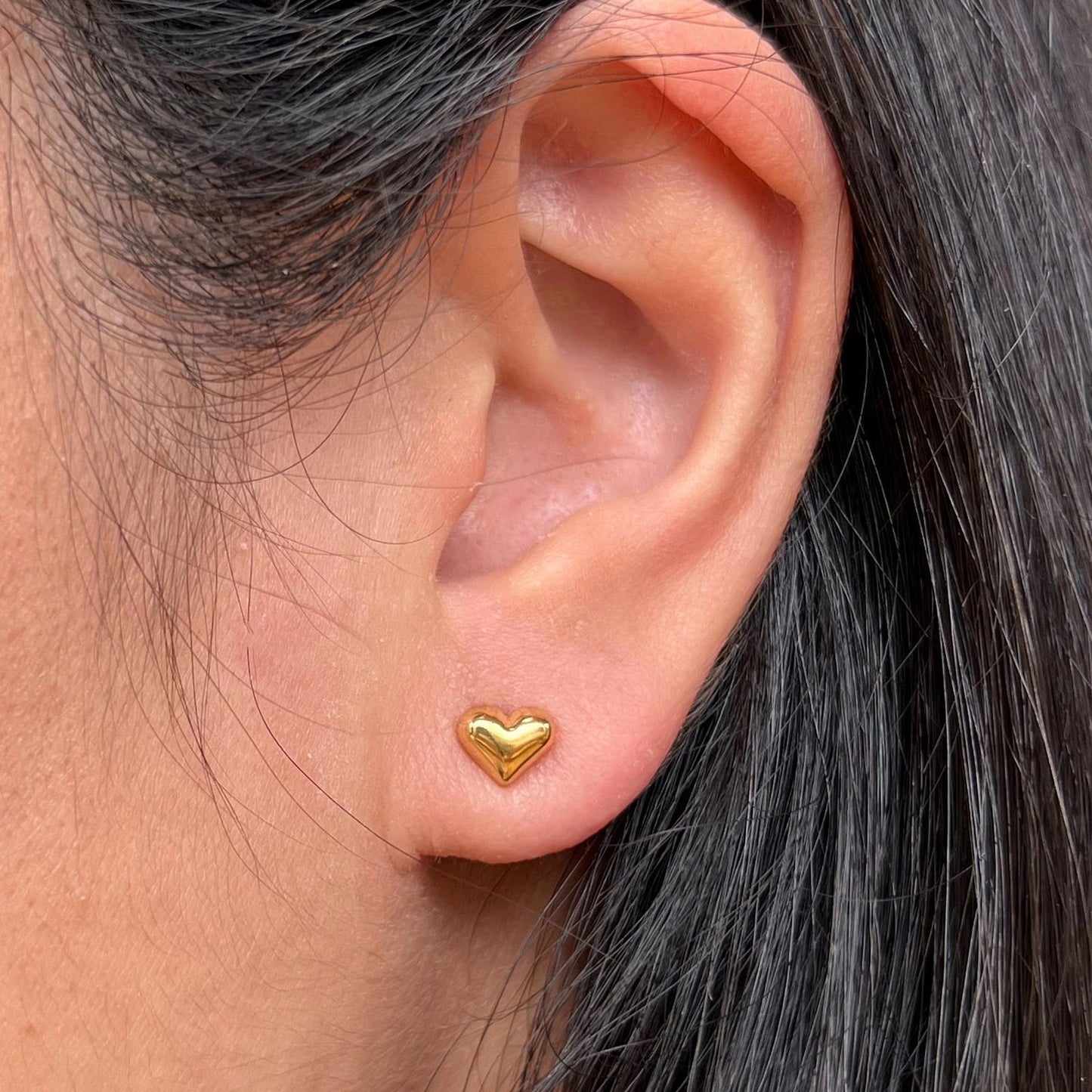 Boucles d'oreilles "Tendre discrétion" de Visée, en forme de cœur en acier doré, portées à l'oreille.