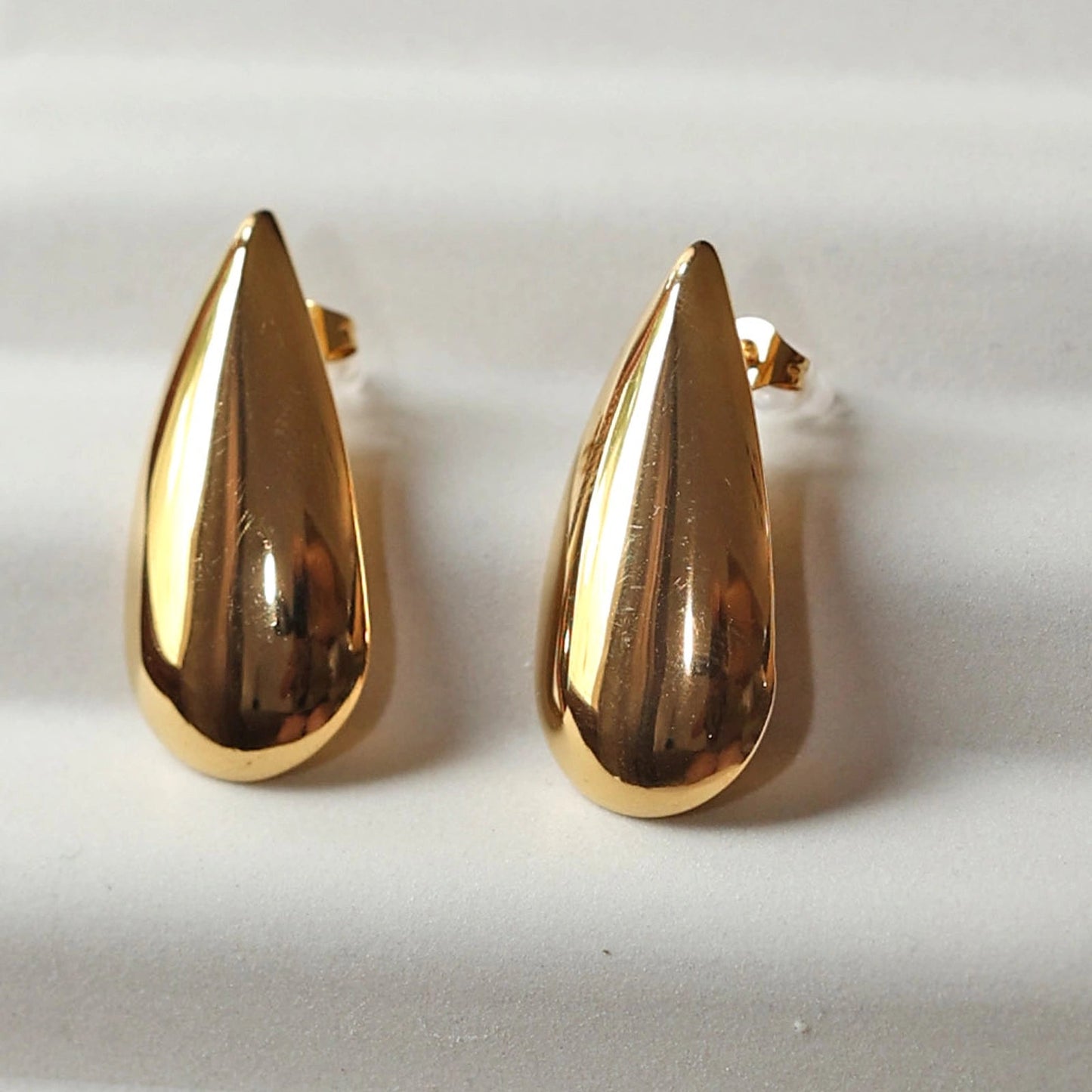 Boucles d'oreilles Larmes assumées en acier doré, gouttes lumineuses capturées en gros plan.