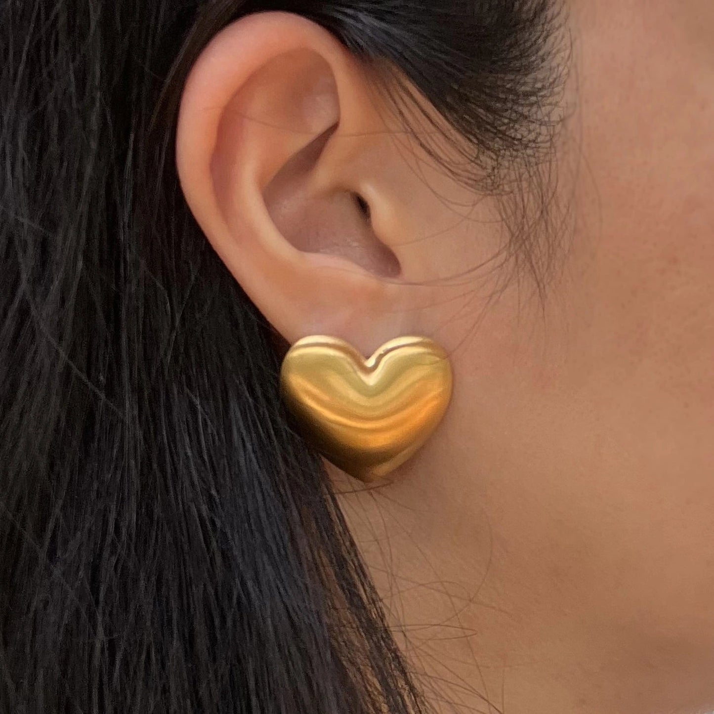 Boucles d'oreilles "S'aimer", en maxi cœurs dorés mat, en acier Inoxydable, portées à l'oreille.