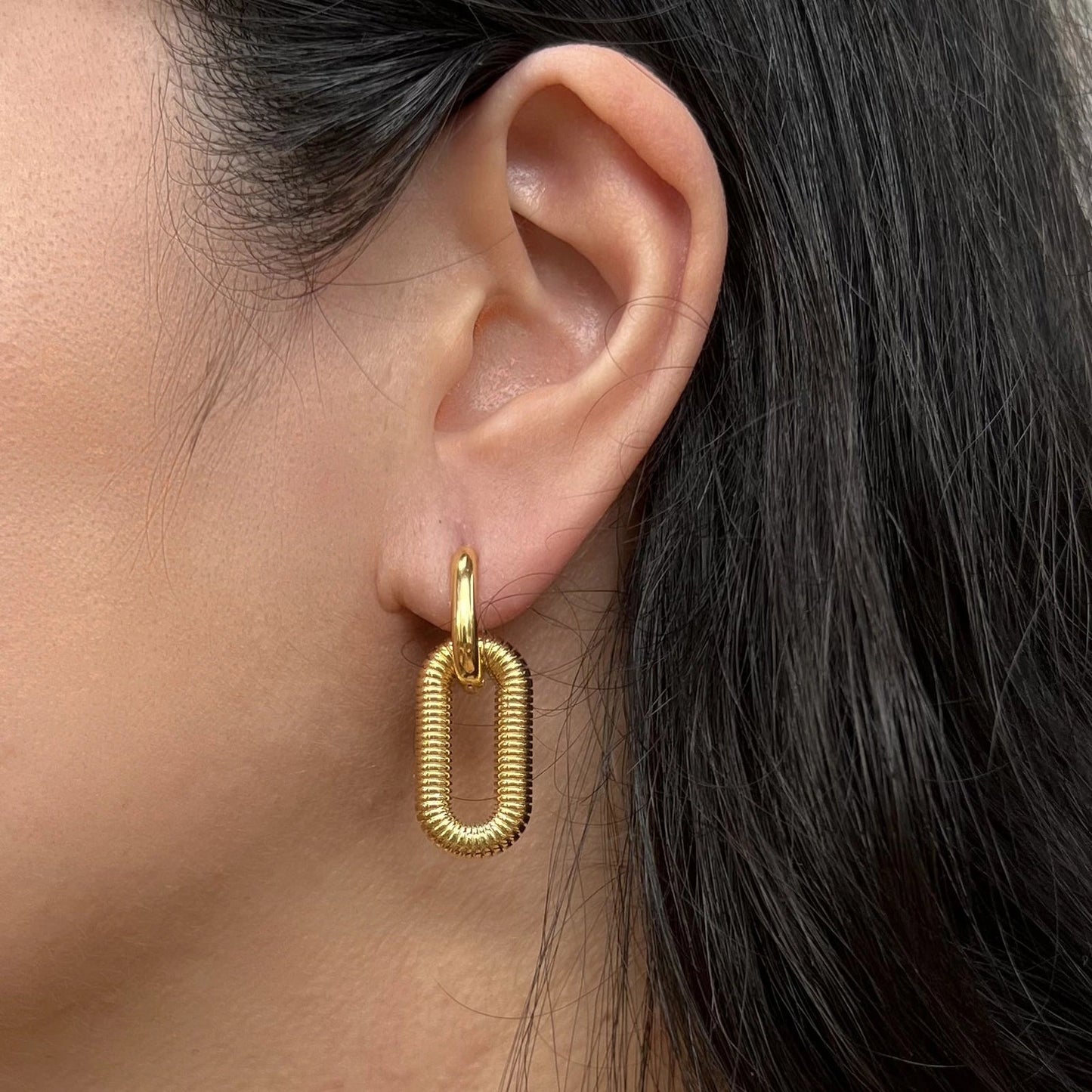 Boucles d'oreilles "J'existe" en acier doré, au design modulable, portées à l'oreille.
