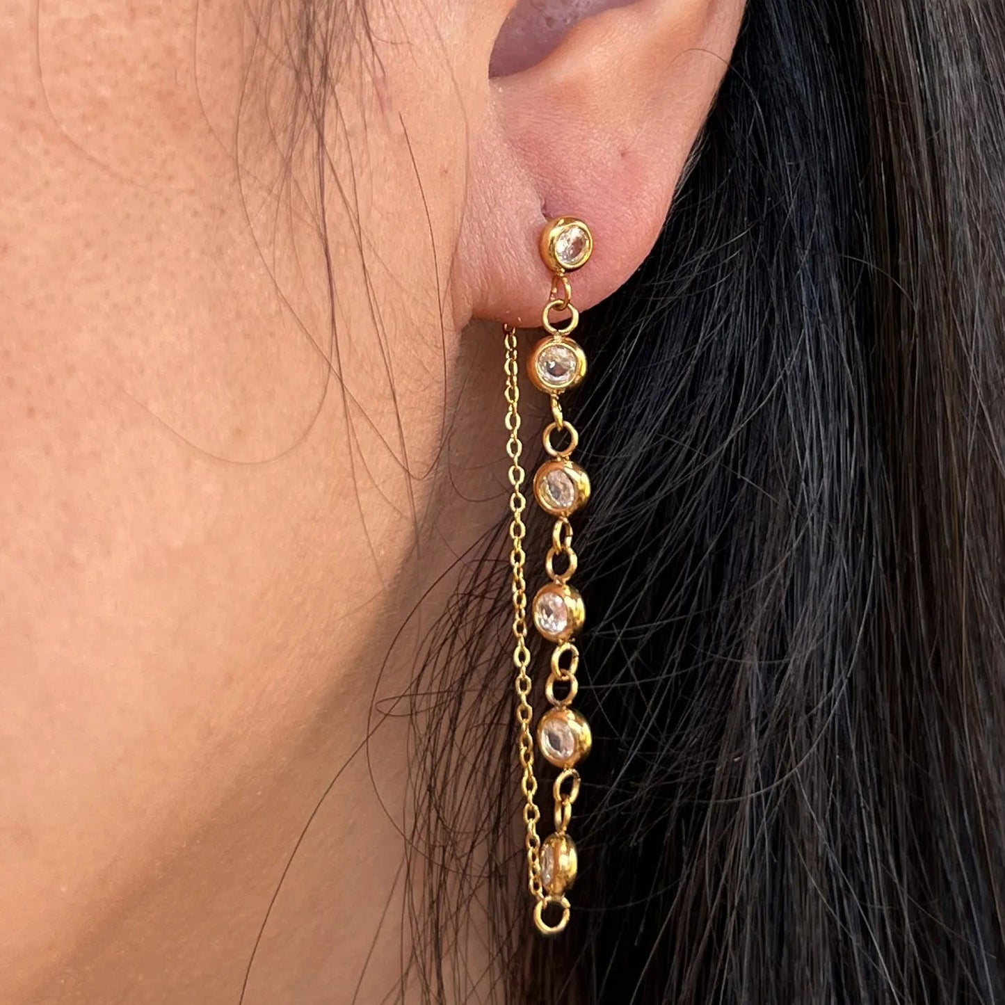 Boucles d'oreilles dorées Eclat en acier inoxydable, pendantes et serties de strass brillants. Vue portée à l'oreille.