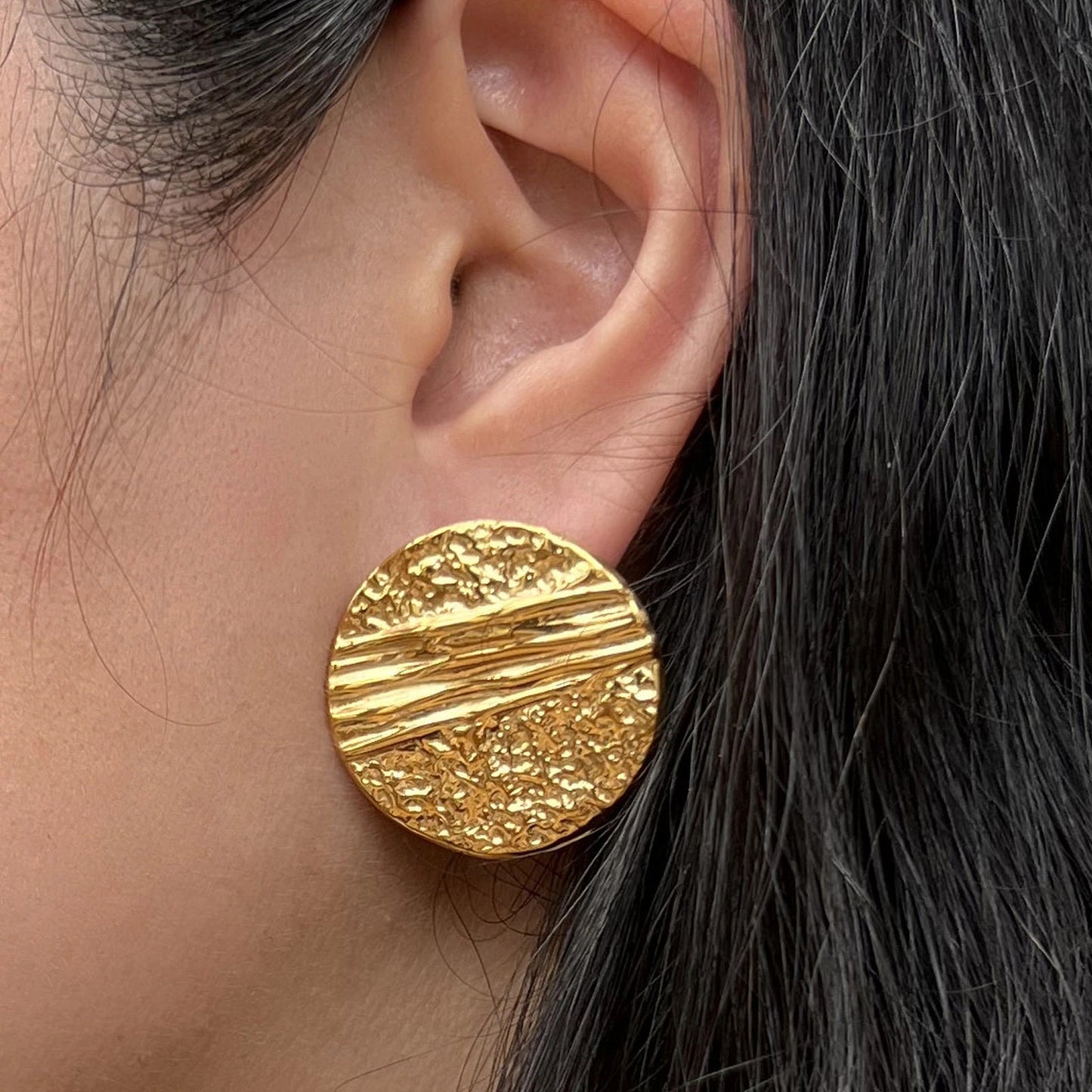 Boucles d'oreilles Rayonnante, en acier inoxydable doré, au design rond texturé et éclatant. Portées à l'oreille.