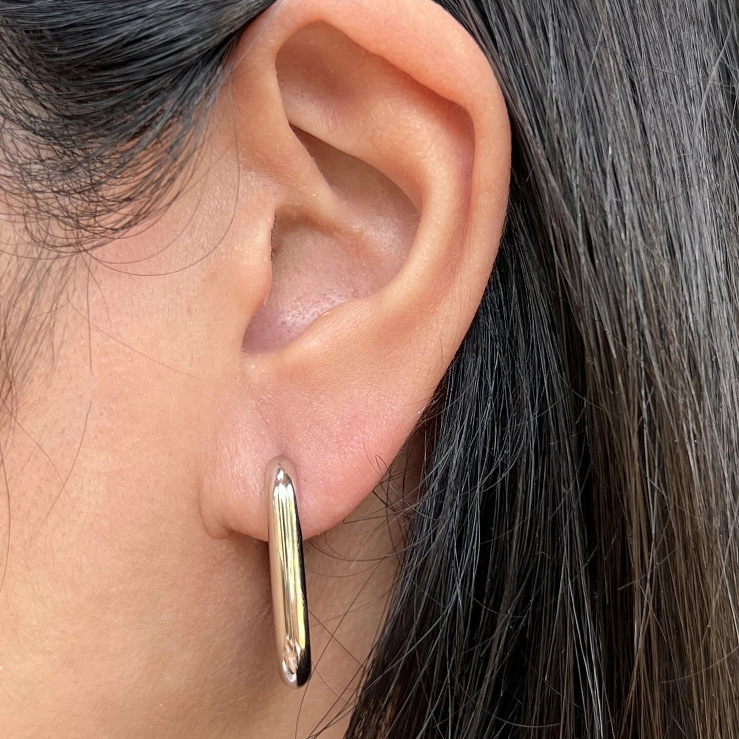 Boucles d'oreilles J'agis, créoles rectangulaires en acier inoxydable argenté, portées sur l'oreille.
