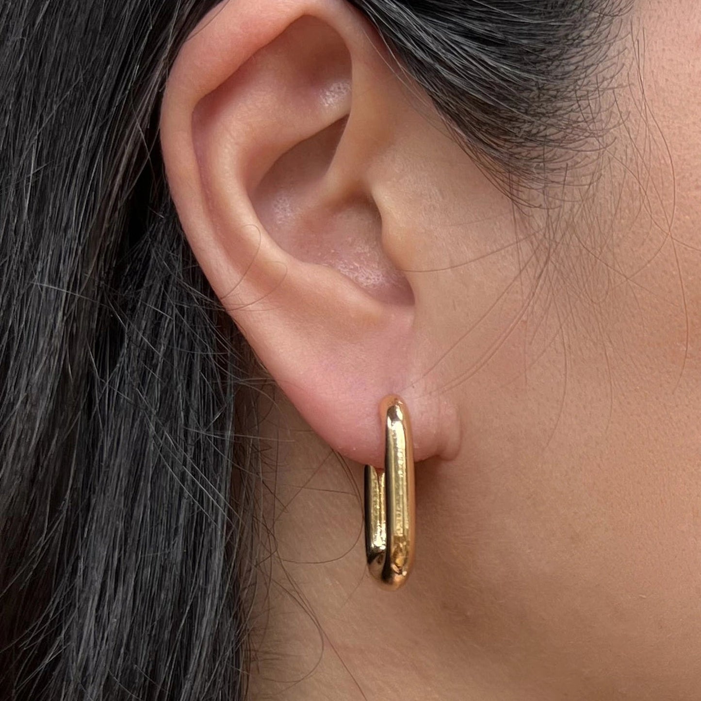 Boucles d'oreilles J'agis, créoles rectangulaires en acier inoxydable doré, portées sur l'oreille.