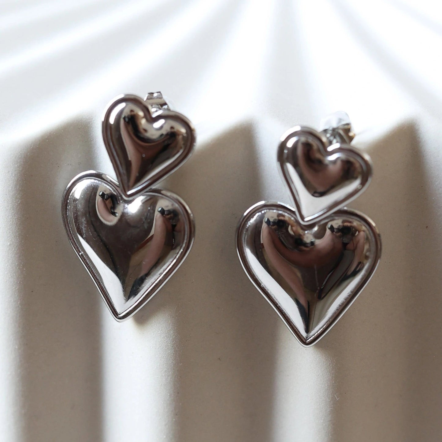 Gros plan sur les boucles d'oreilles "Elle m'a dit" en forme de double coeur, en acier argenté.