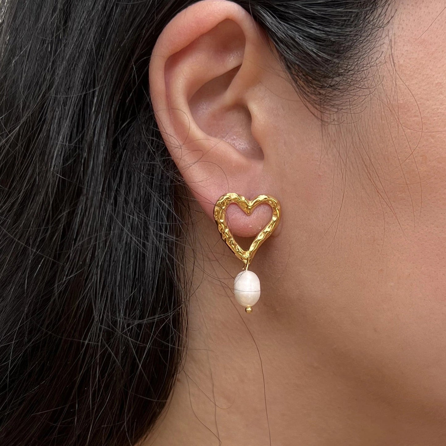 Boucles d’oreilles Loyale, en forme de cœur doré avec perle blanche, en acier inoxydable, portées sur une oreille - vue portée par Visée Bijoux.