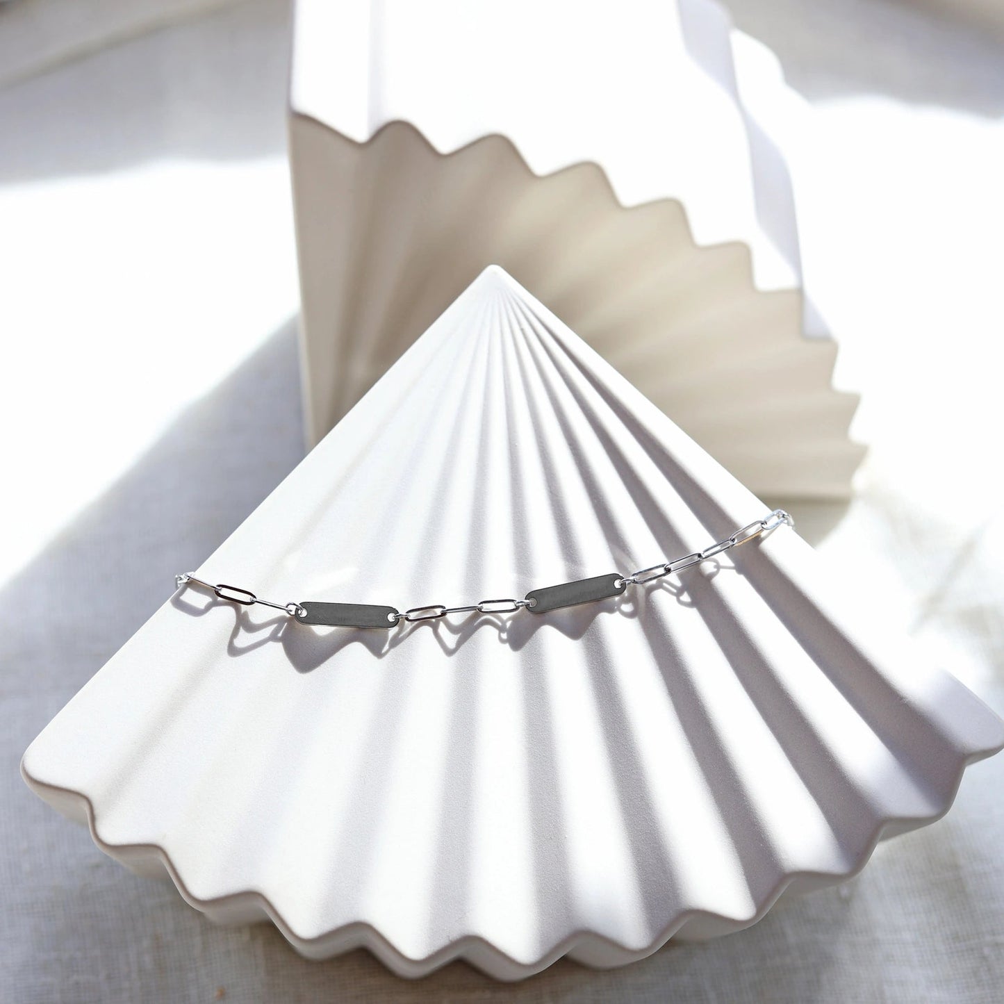 Bracelet "Expression" en acier inoxydable argenté, à personnaliser avec deux plaques gravables, présenté sur un fond beige texturé.