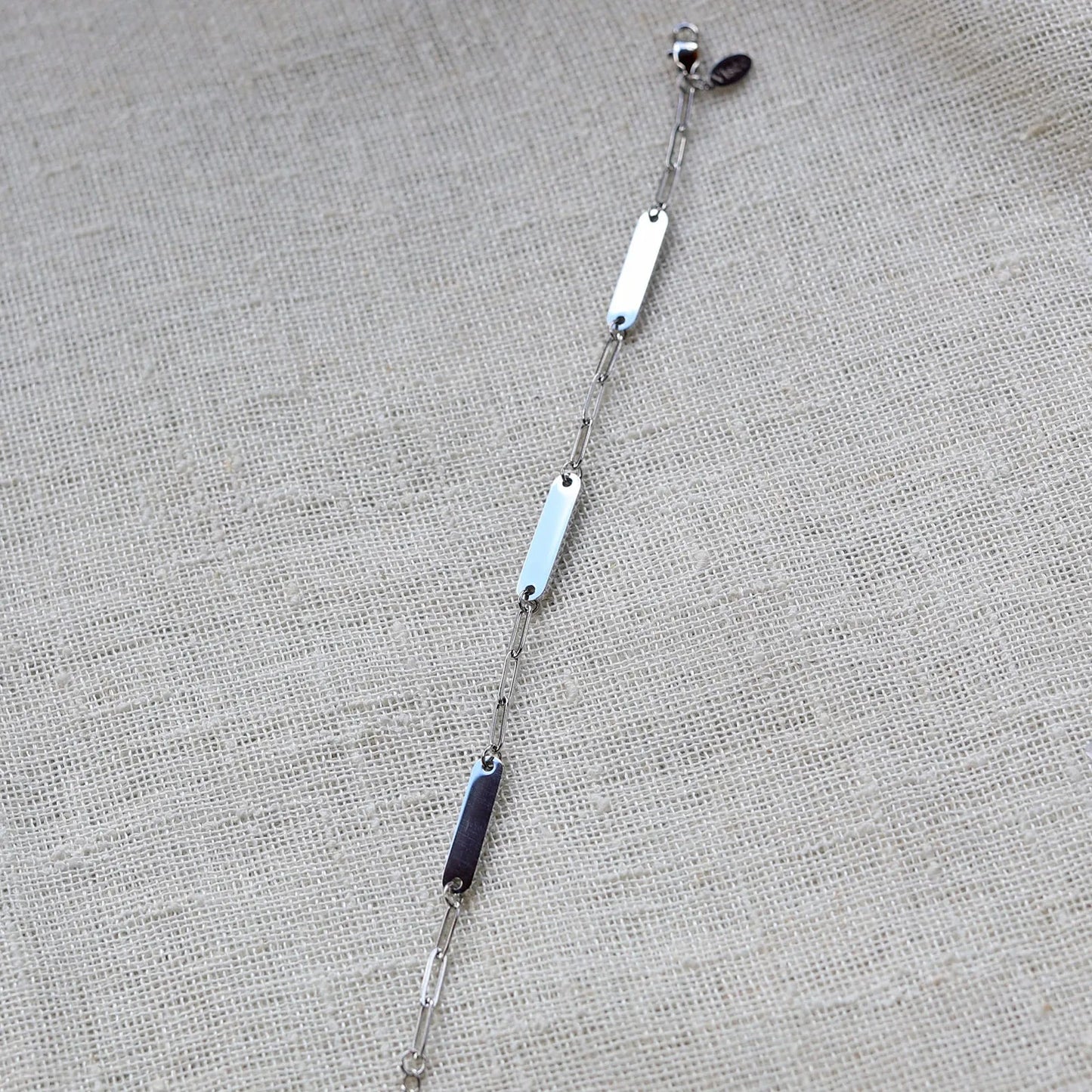 Bracelet "Expression" en acier inoxydable argenté, à personnaliser avec trois plaques gravables, présenté sur un fond beige texturé.