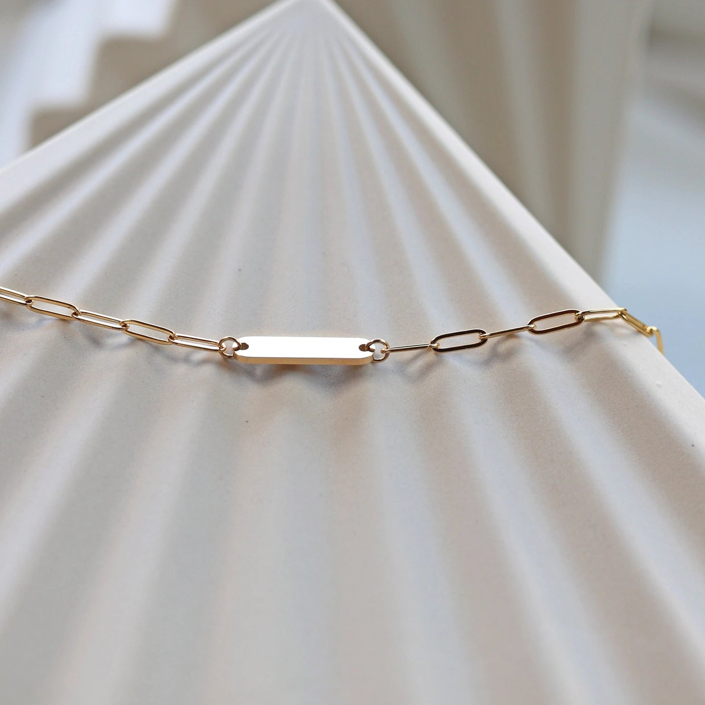 Bracelet "Expression" en acier inoxydable doré, à personnaliser avec une plaque gravable, présenté sur un fond beige texturé.