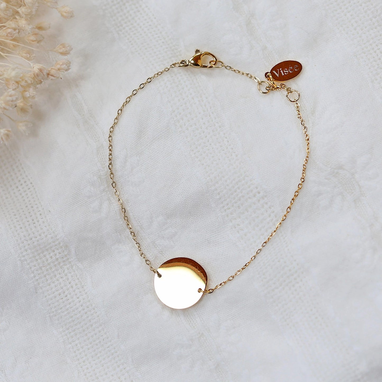 Bracelet "Confiance" en acier doré personnalisable avec médaille ronde, présenté sur un tissu beige texturé.