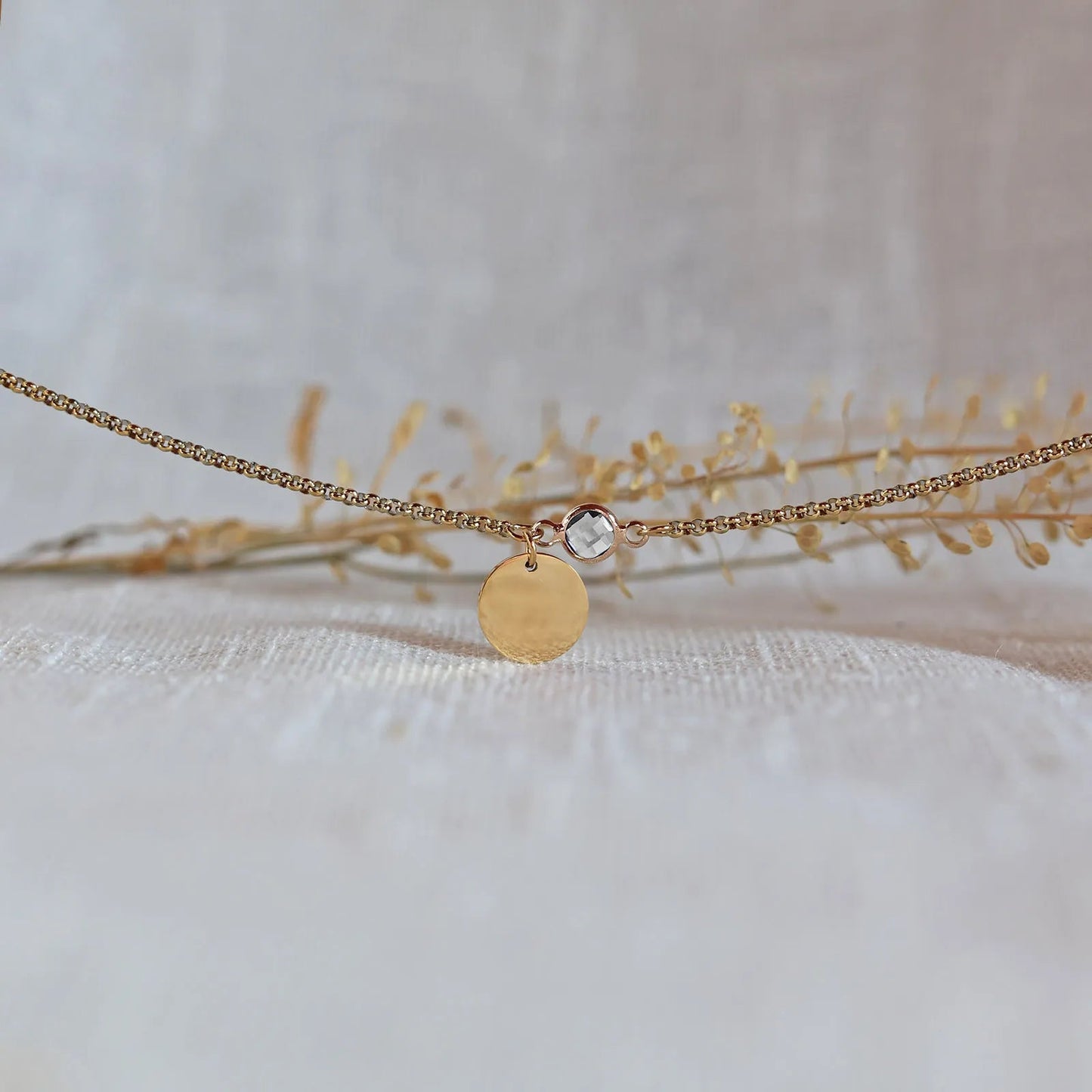 Bracelet "Mon choix" avec médaillon doré personnalisable et pierre blanche, posé sur un fond beige texturé.