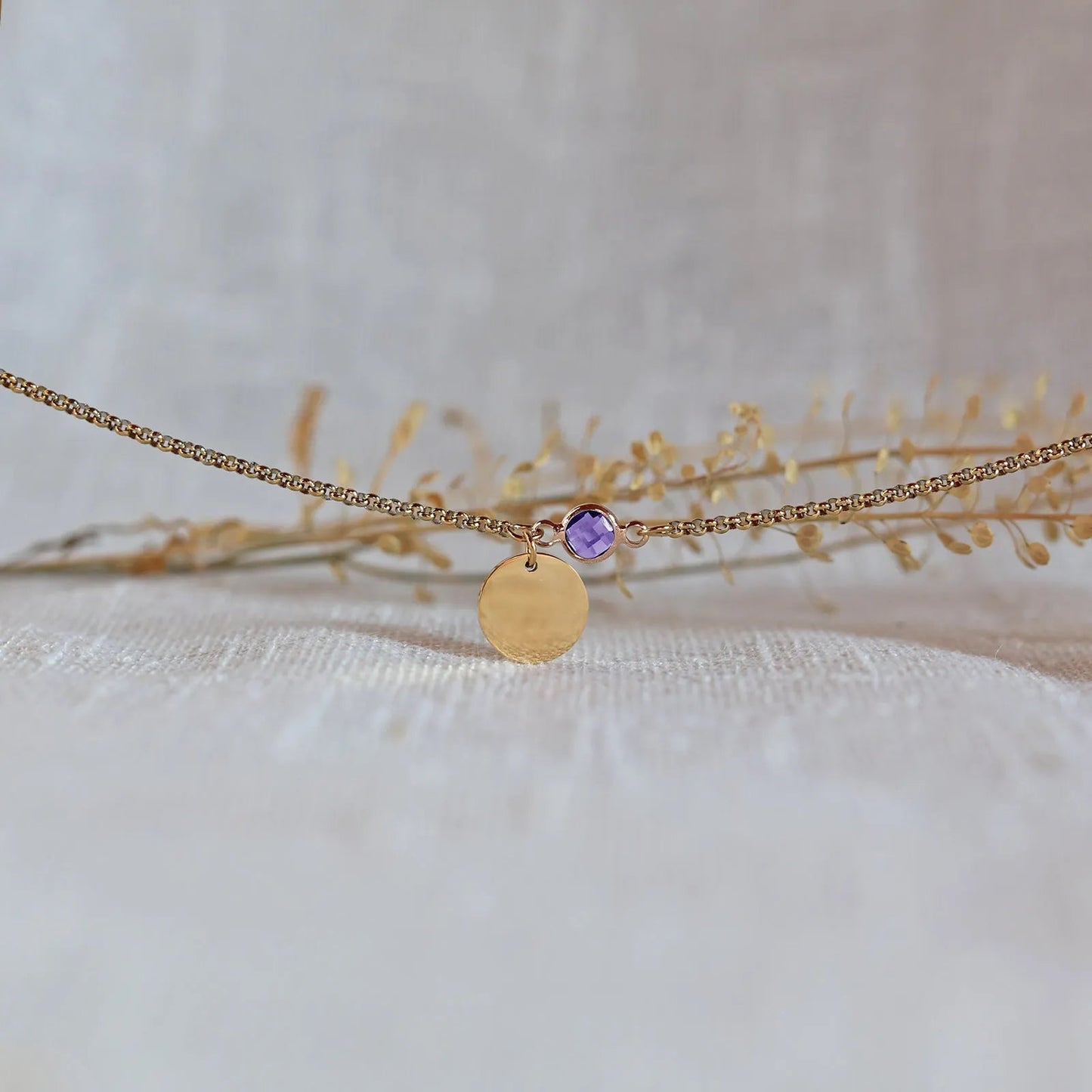 Bracelet "Mon choix" avec médaillon doré personnalisable et pierre violette, posé sur un fond beige texturé.