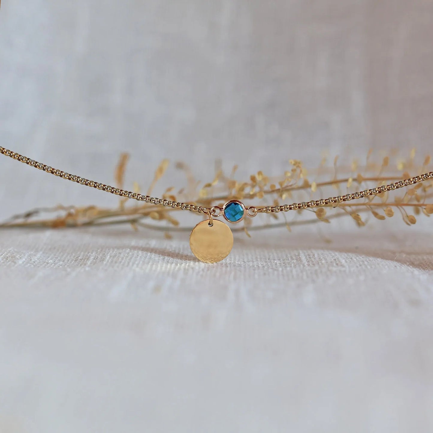 Bracelet "Mon choix" avec médaillon doré personnalisable et pierre bleu turquoise, posé sur un fond beige texturé.
