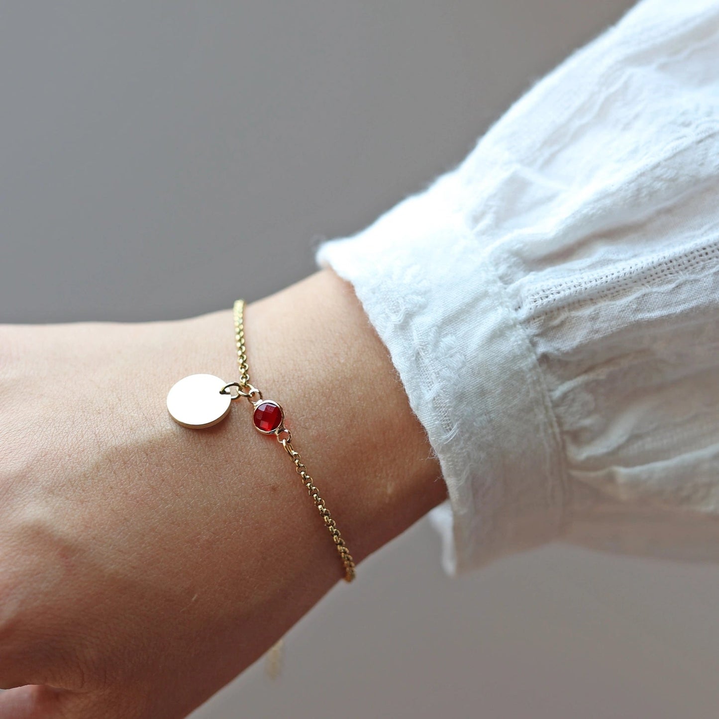 Bracelet "Mon choix" avec médaillon doré personnalisable et pierre rouge, porté autour du poignet.