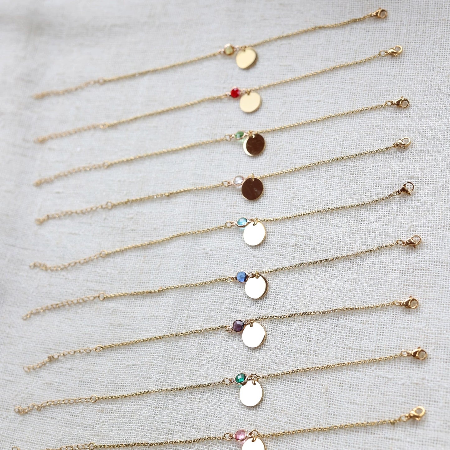 Vue d'ensemble des bracelets "Mon choix" avec médaillon doré personnalisable et pierre de couleur, posés sur un fond beige texturé.