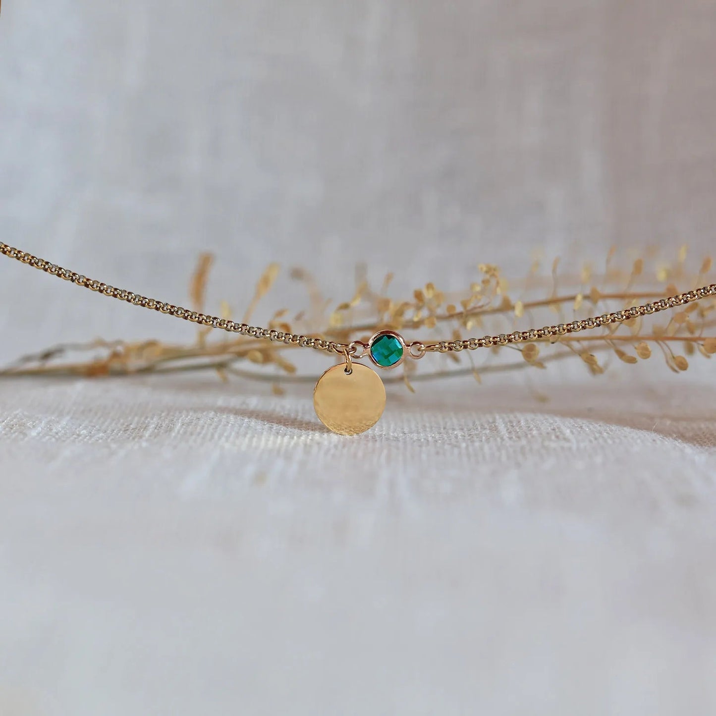 Bracelet "Mon choix" avec médaillon doré personnalisable et pierre vert émeraude, posé sur un fond beige texturé.