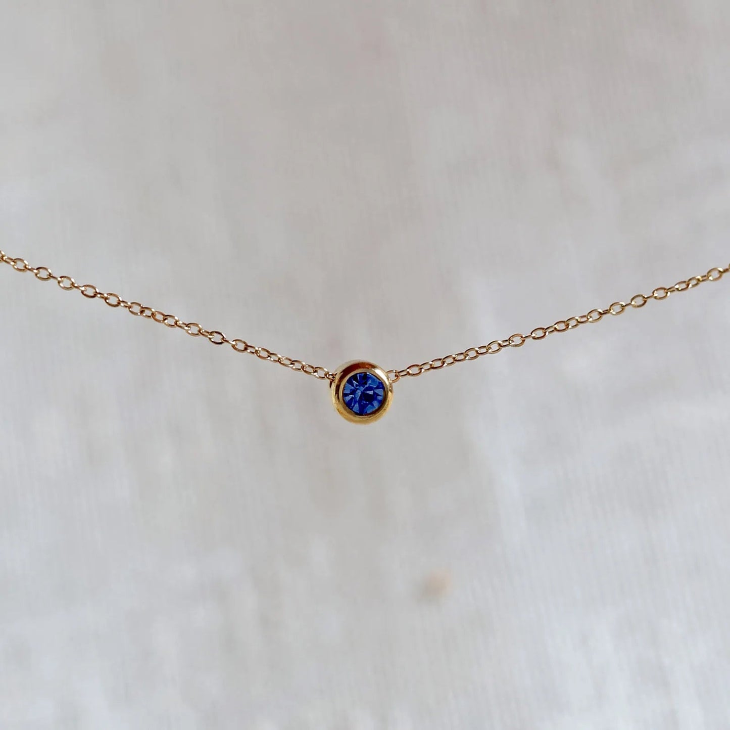 Bracelet "Mon intérieur" en acier doré, orné d'une pierre bleue roi coulissante personnalisable, posé sur un fond beige.