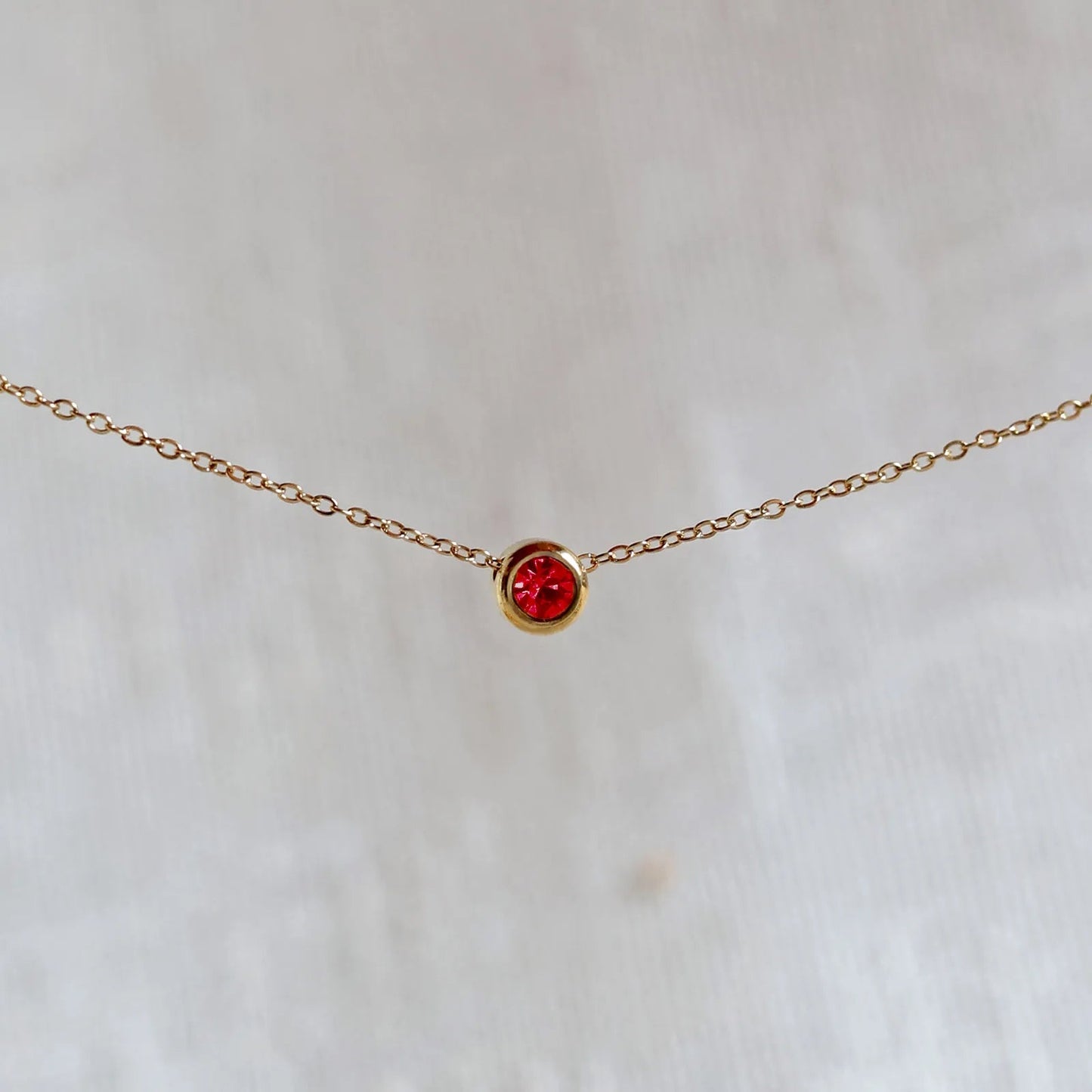 Bracelet "Mon intérieur" en acier doré, orné d'une pierre rouge coulissante personnalisable, posé sur un fond beige.
