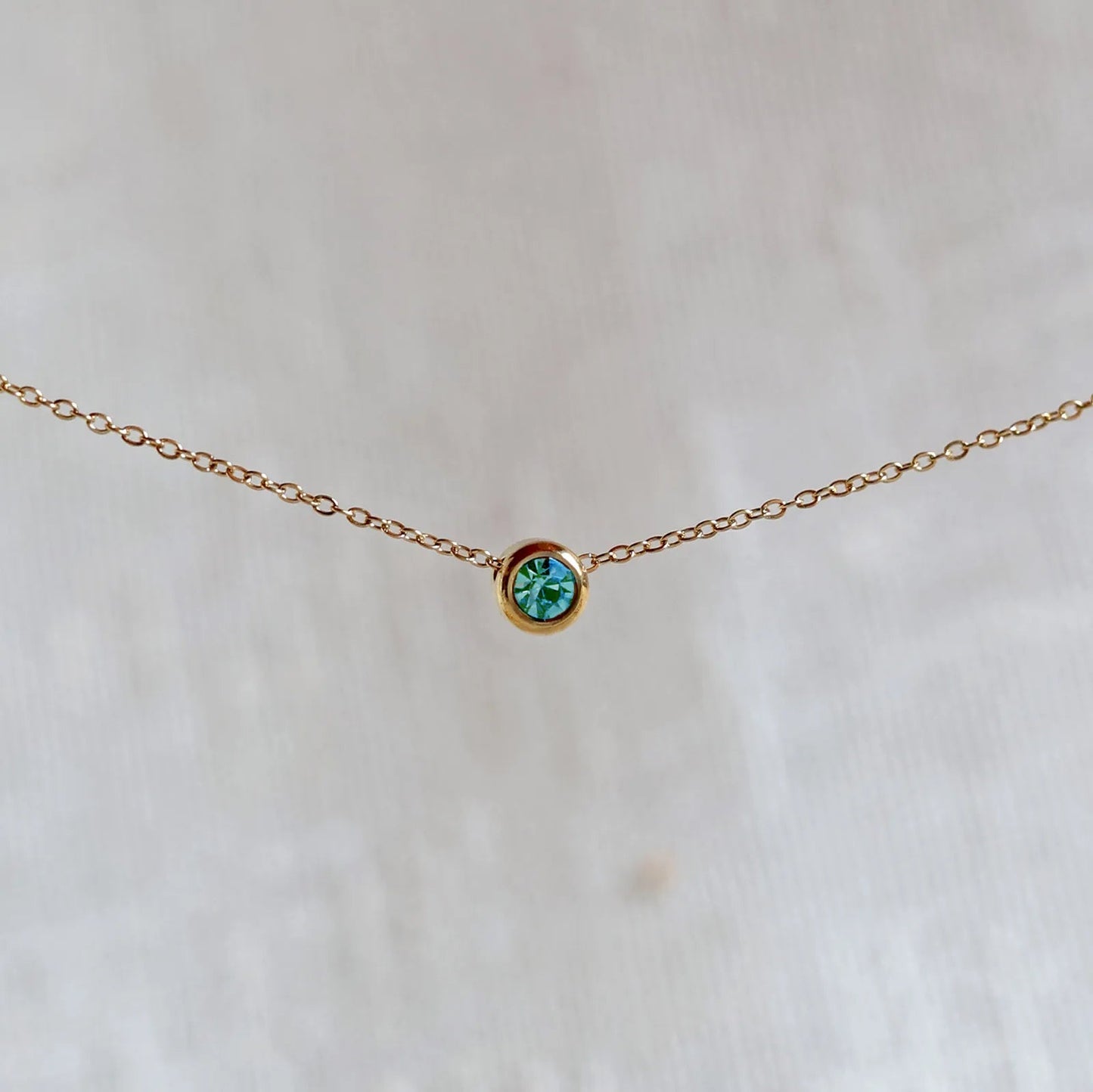 Bracelet "Mon intérieur" en acier doré, orné d'une pierre turquoise coulissante personnalisable, posé sur un fond beige.