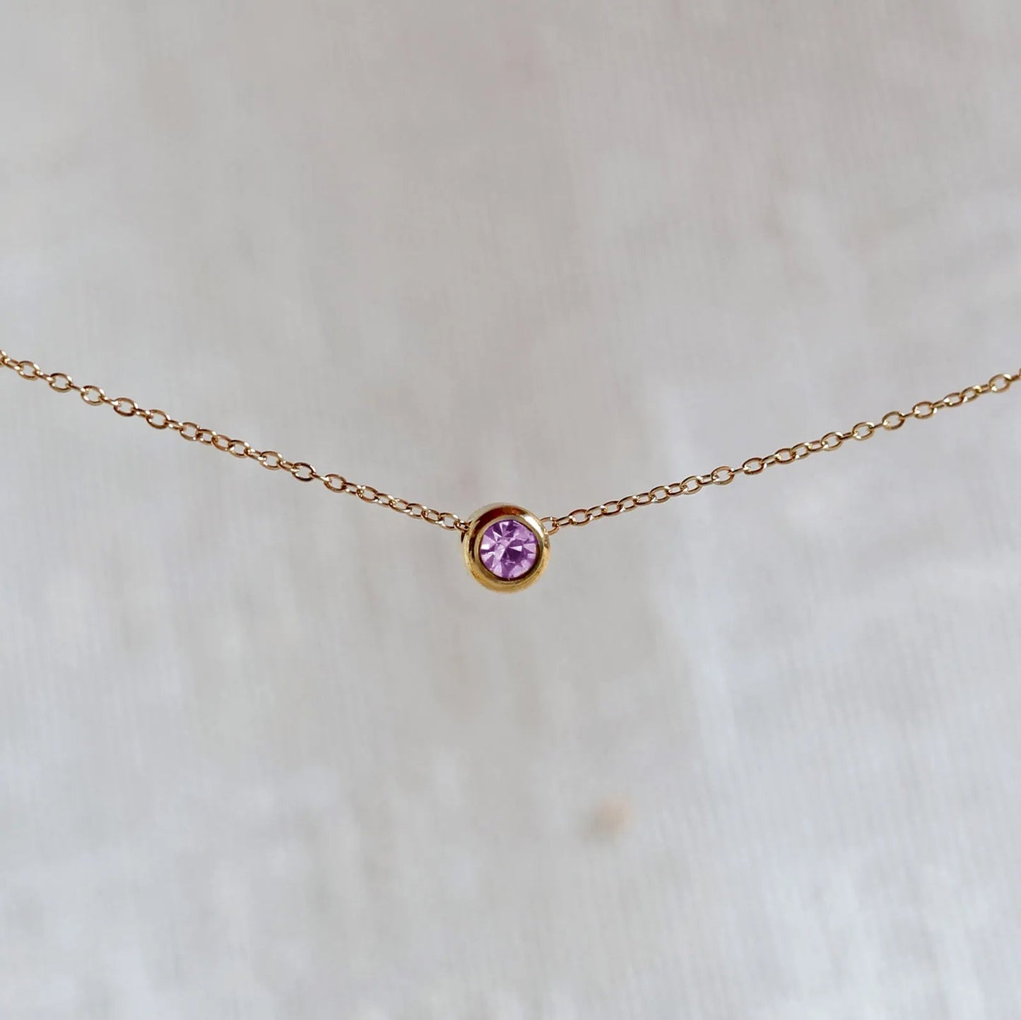Bracelet "Mon intérieur" en acier doré, orné d'une pierre violette coulissante personnalisable, posé sur un fond beige.
