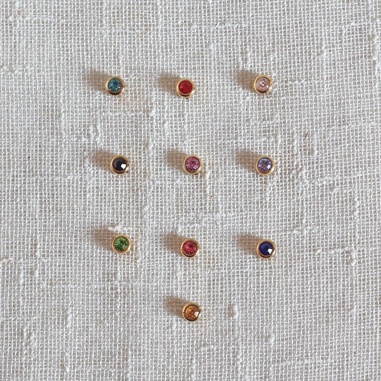 Pierres colorées en acier doré, posées sur un fond beige texturé.