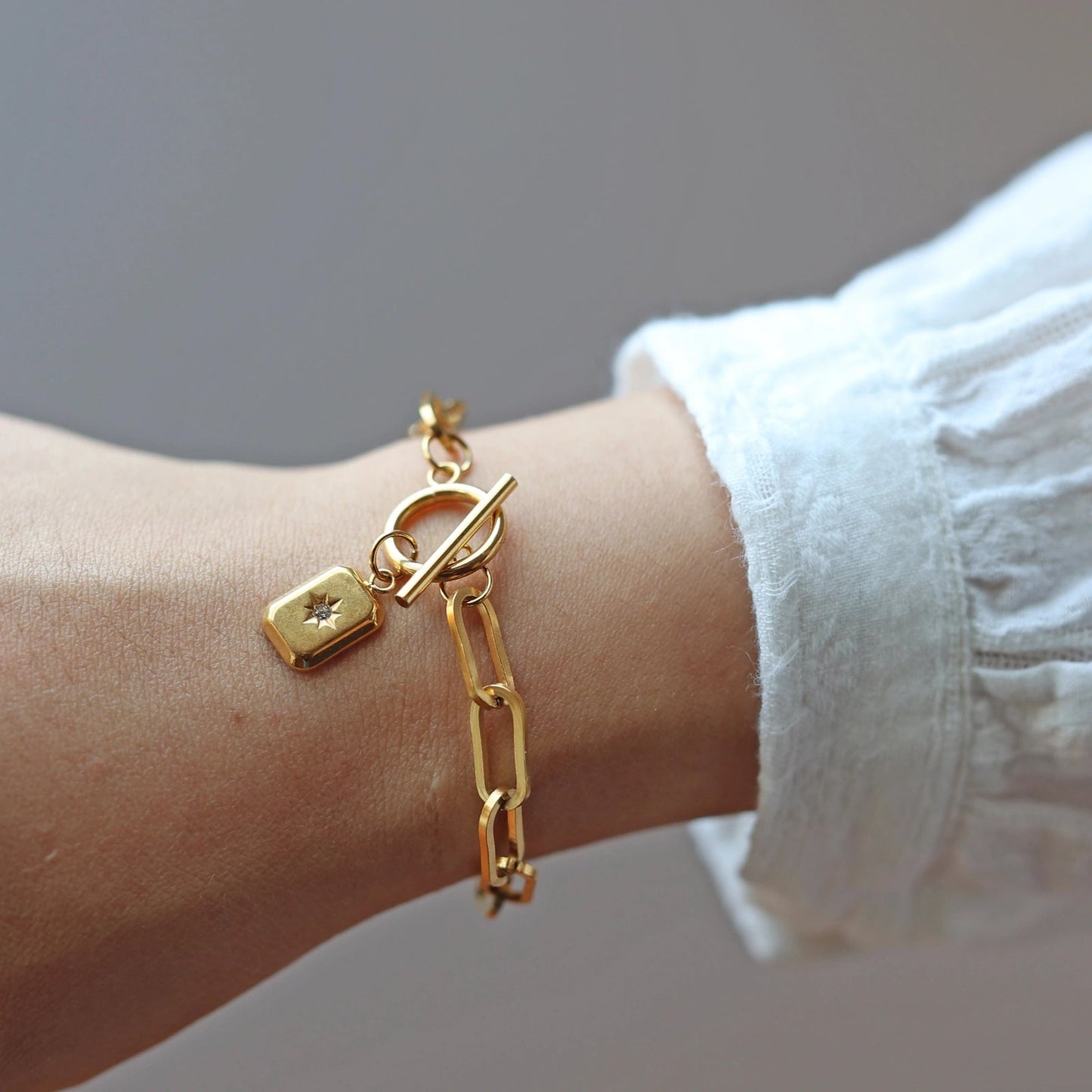 Bracelet "Révélation" en acier doré avec breloque rectangulaire personnalisable, porté autour du poignet.