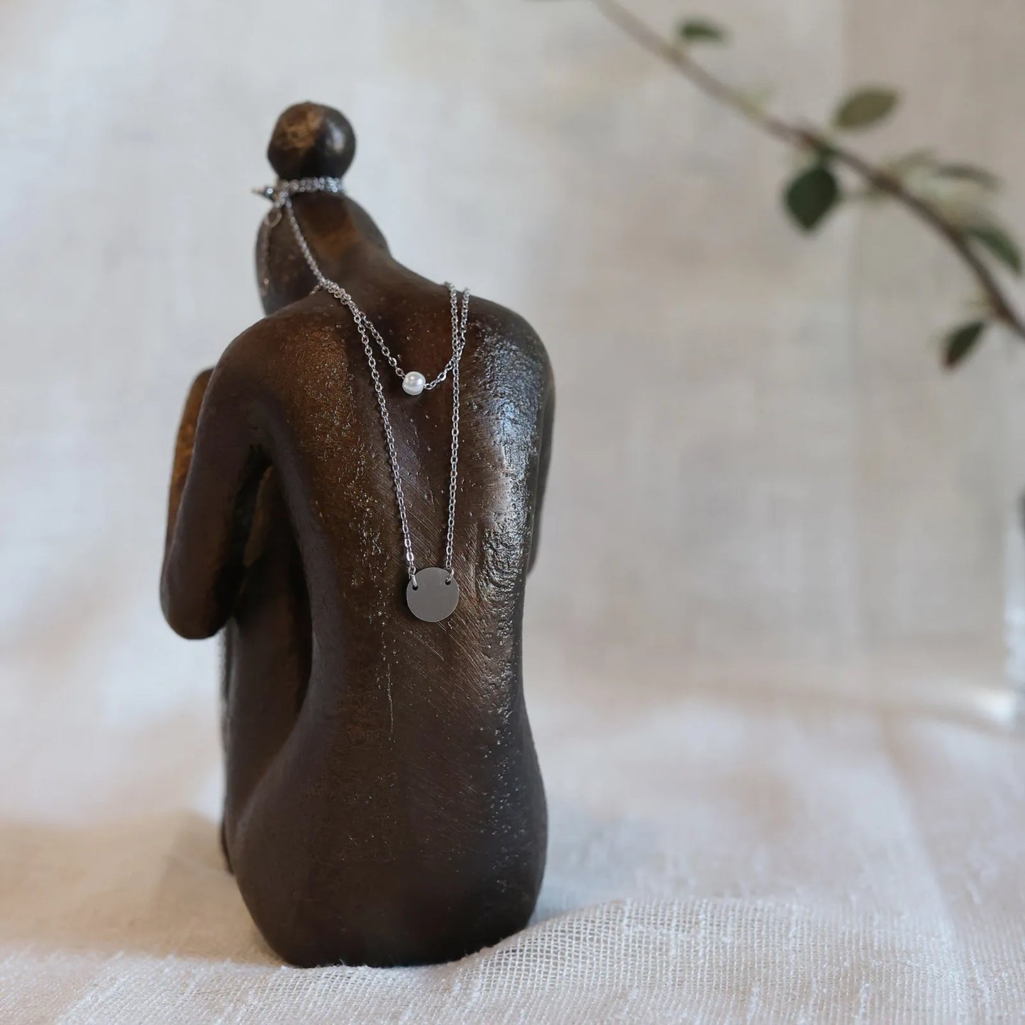 Double collier "Je me choisis" composé d'une perle et d'un médaillon en acier argenté, porté sur une statue de femme vue de dos.