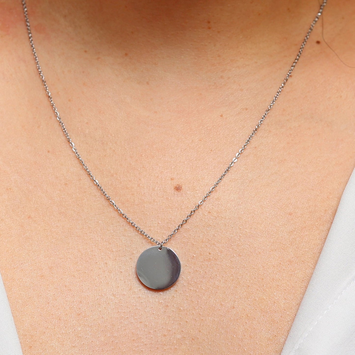 Collier "Reflet" avec médaille ronde personnalisé en acier inoxydable argenté, porté autour du cou.