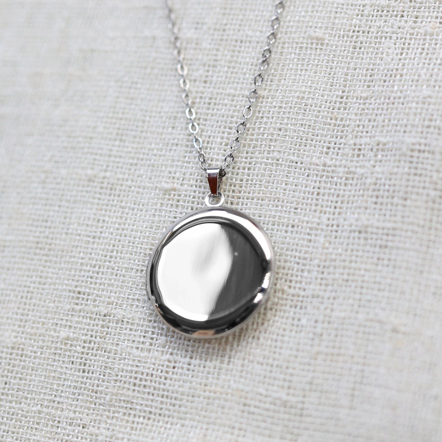 Gros plan sur le collier "Ce jour là" avec médaillon rond personnalisable en acier argenté, présenté sur un fond beige texturé.