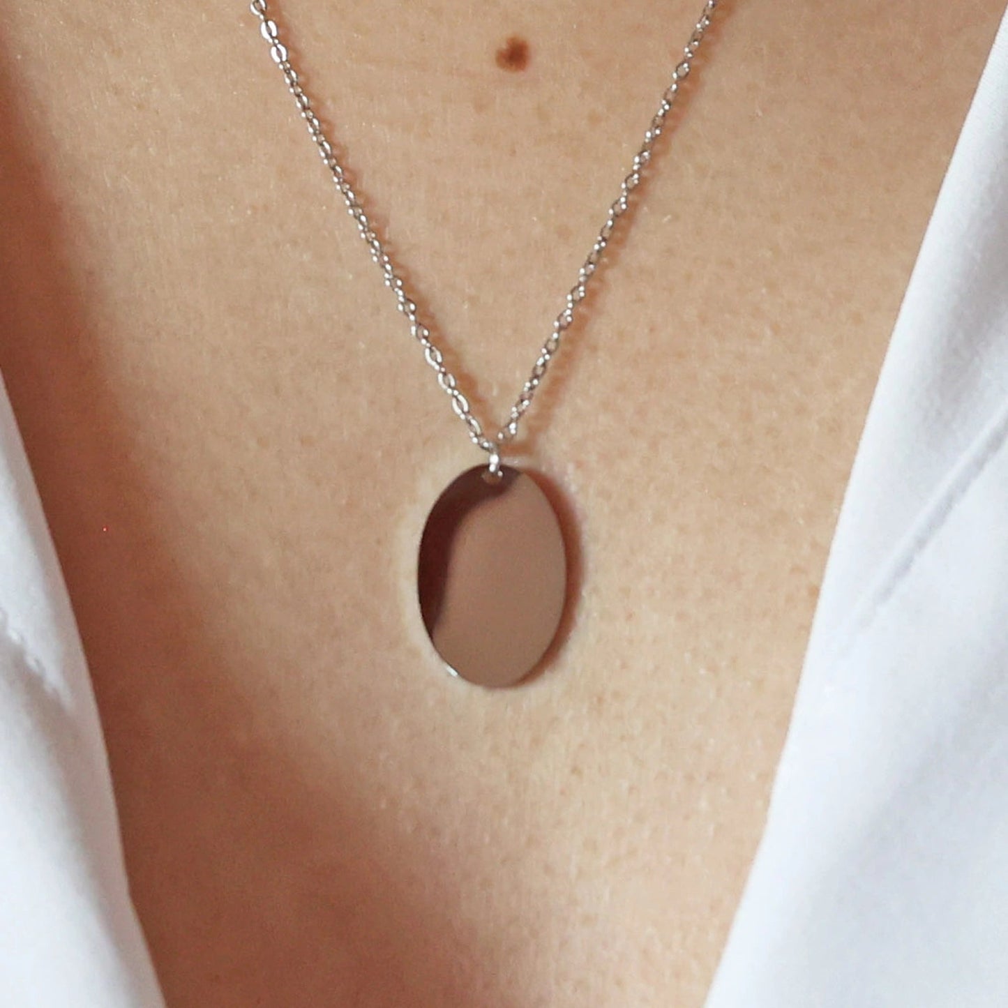 Zoom sur le collier "Tendresse", pendentif ovale personnalisable en acier inoxydable argenté, porté autour du cou.