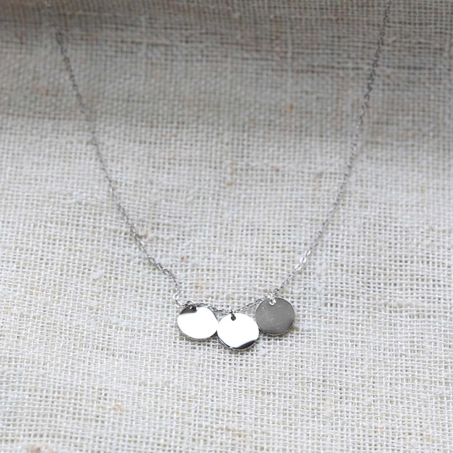Collier "Inspiration" en acier inoxydable argenté, composé de trois médaillons personnalisables, présenté sur un fond beige texturé.