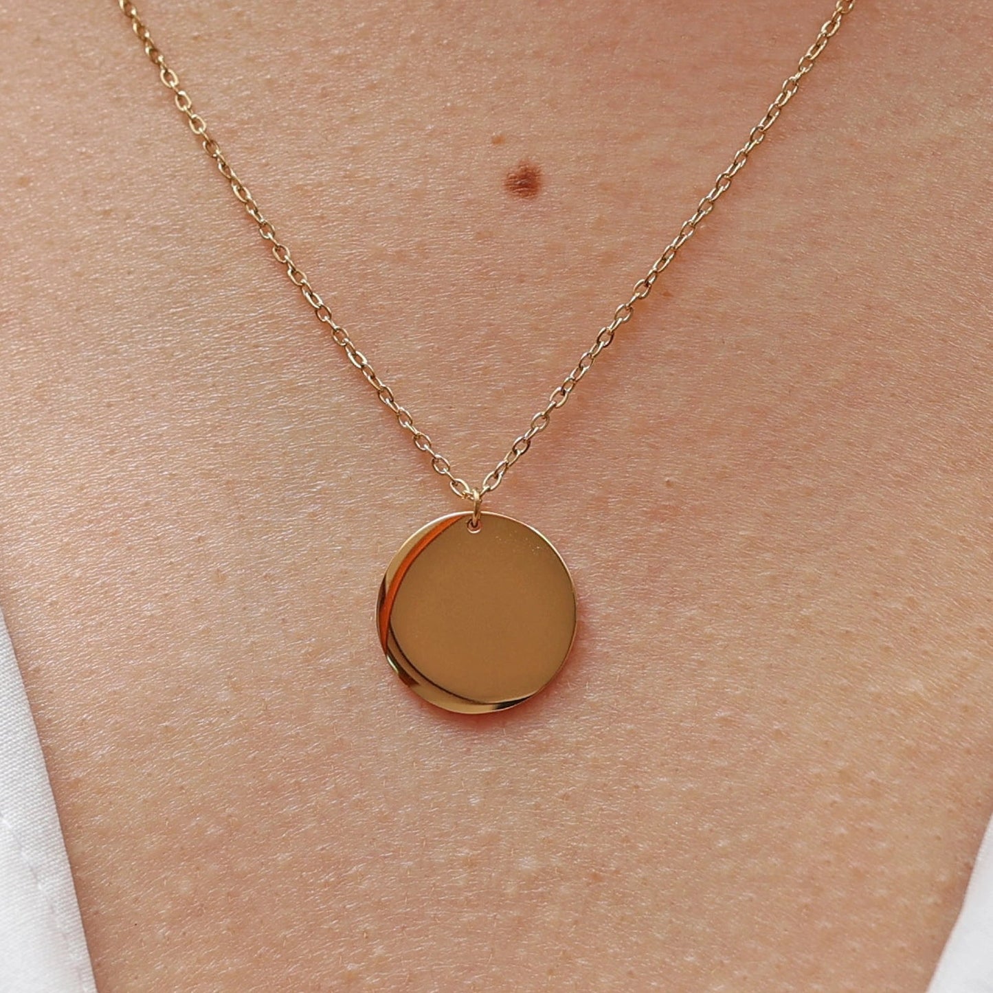 Collier "Reflet" avec médaille ronde personnalisé en acier inoxydable doré, porté autour du cou.