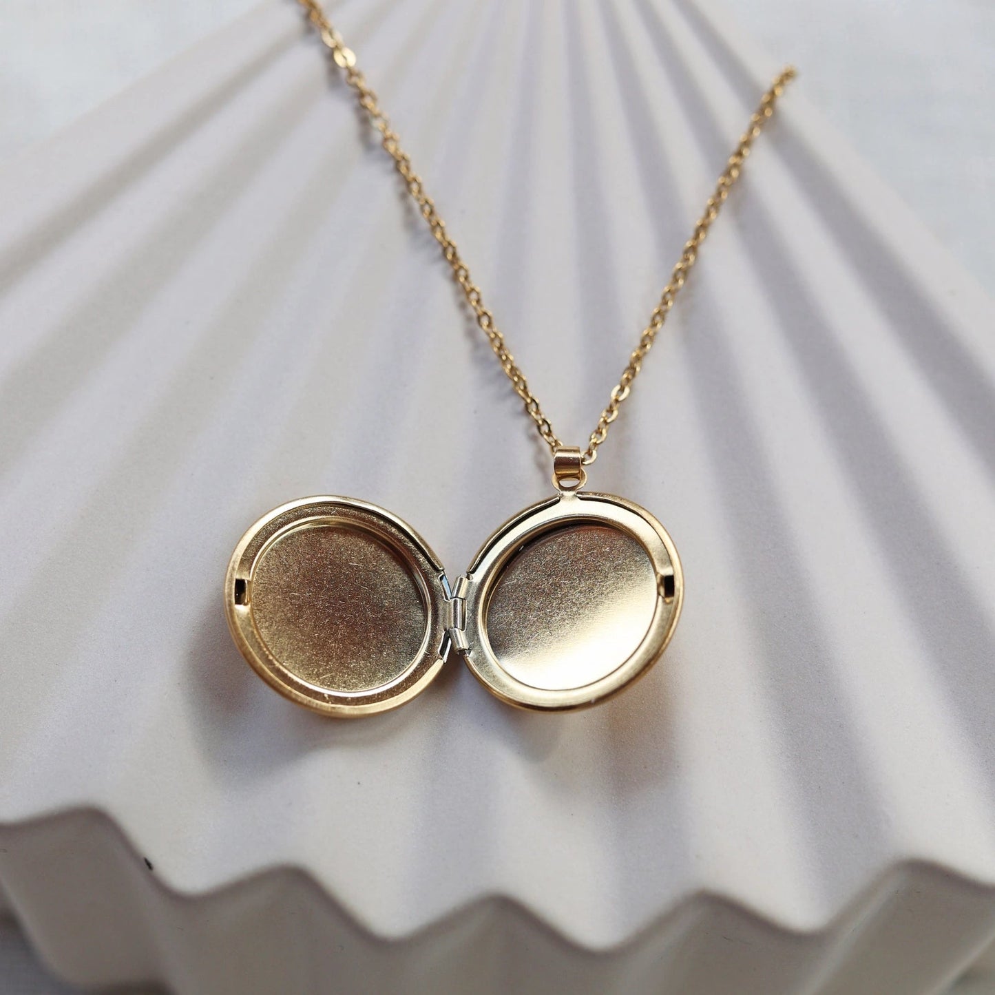 Collier "Ce jour là" avec médaillon rond personnalisable en acier doré, présenté sur un fond beige texturé.