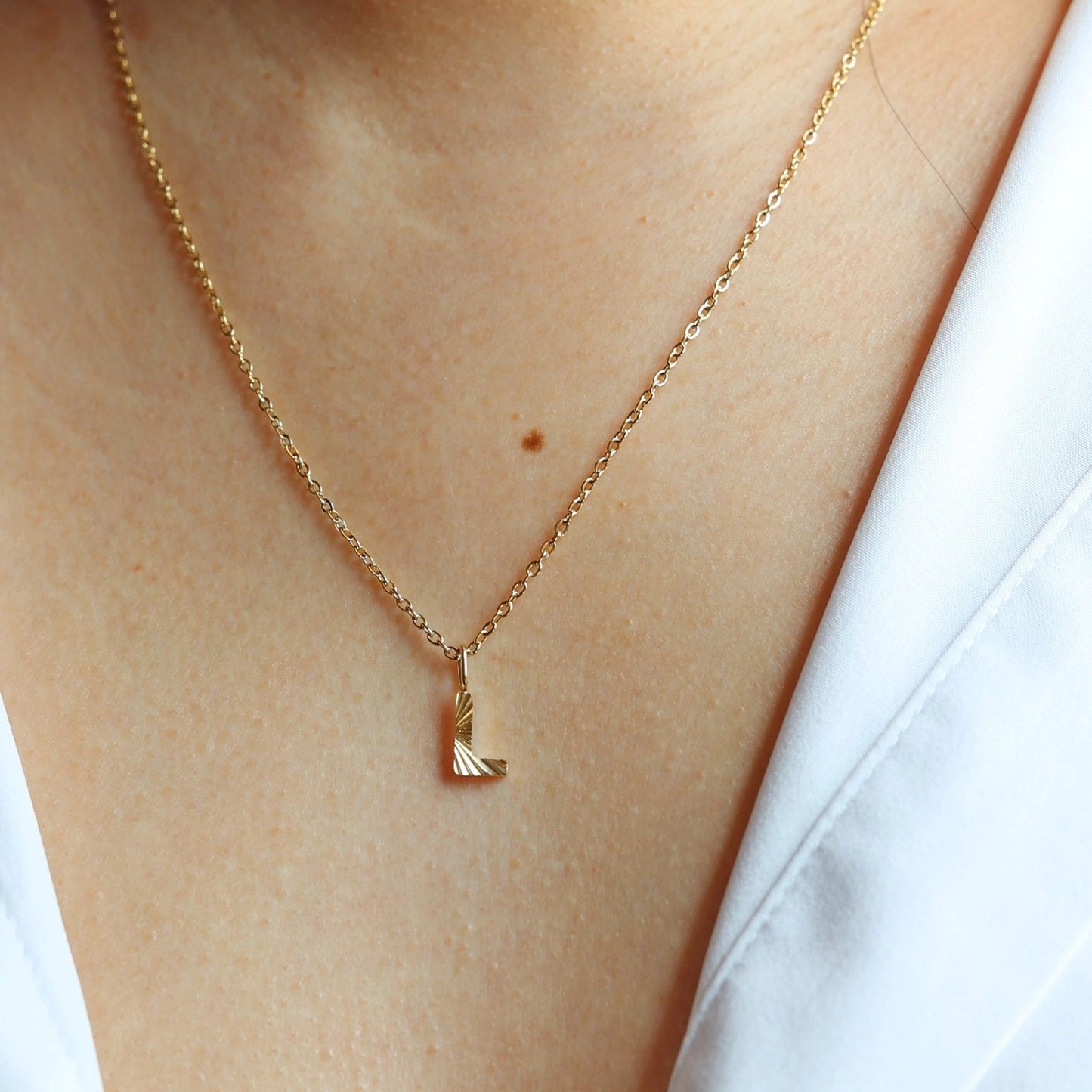 Collier "Je suis" avec pendentif lettre L striée, en acier doré, porté au cou.