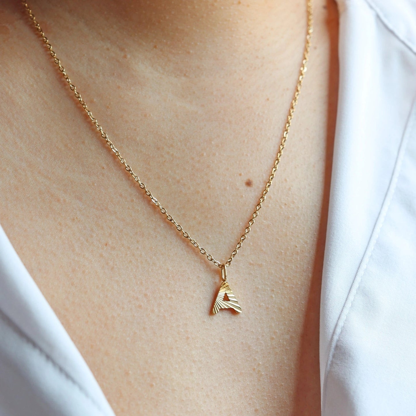 Collier "Je suis" avec pendentif lettre A striée, en acier doré , porté au cou.