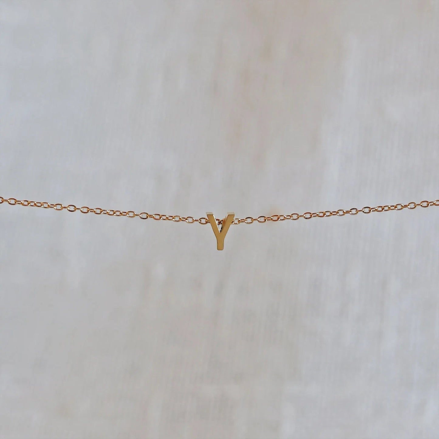 Collier L'instant avec pendentif lettre Y doré en acier inoxydable, suspendu au centre d'une maille fine sur fond beige.