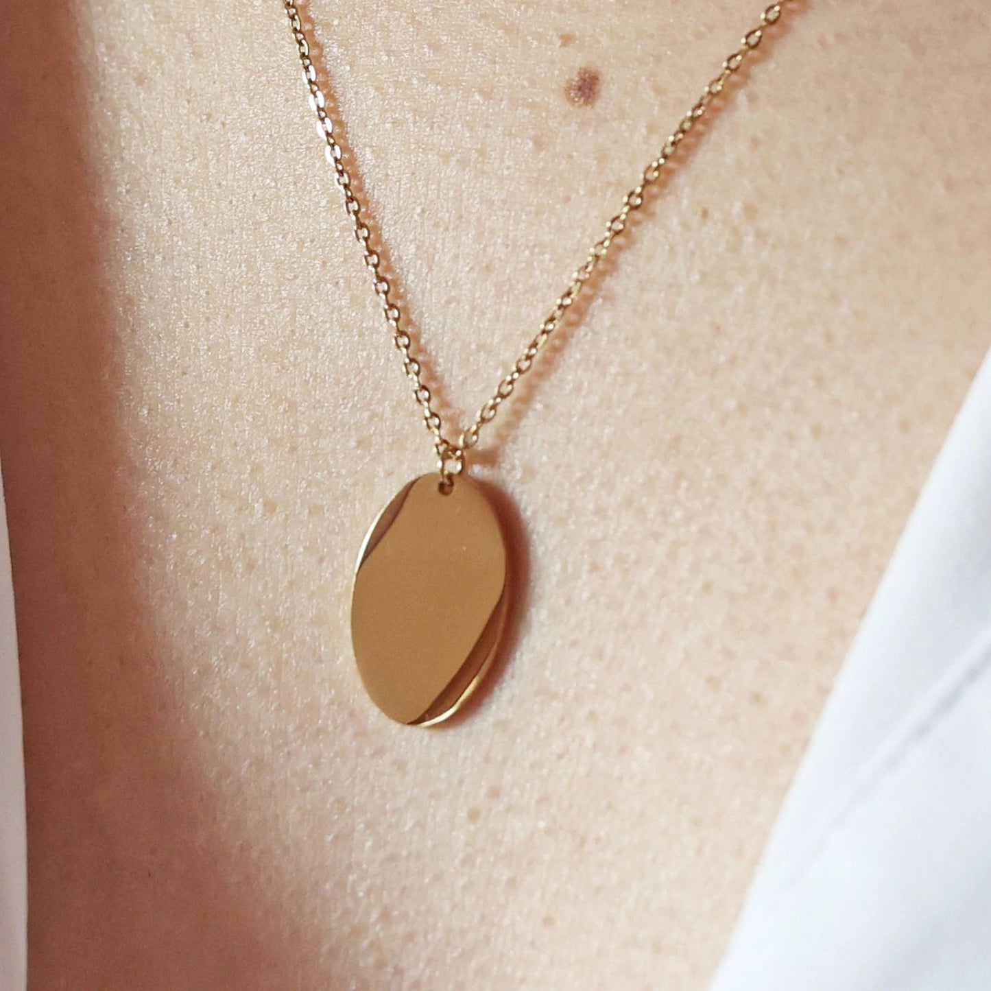 Zoom sur le collier "Tendresse", pendentif ovale personnalisable en acier inoxydable doré, porté autour du cou.