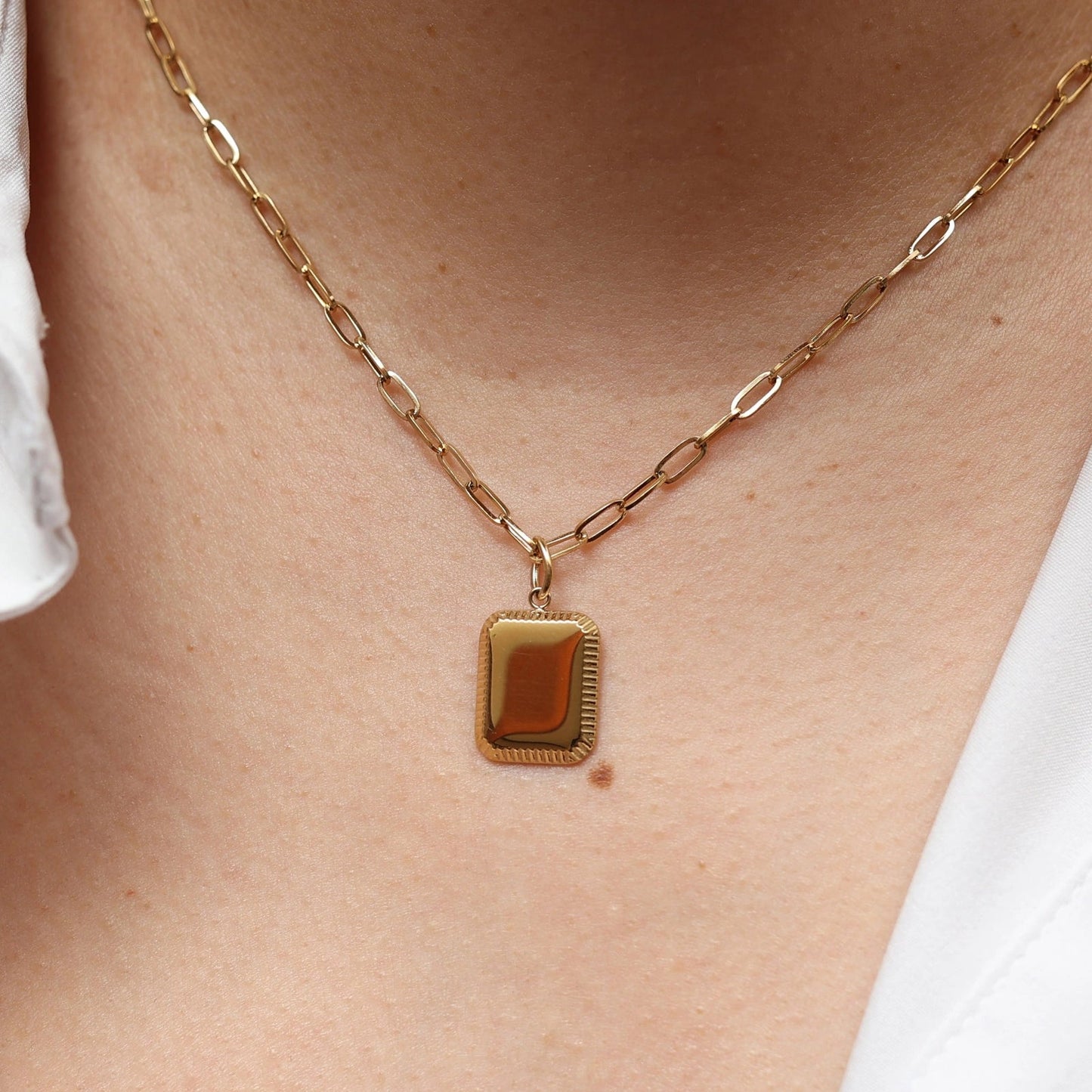 Collier "Ma vérité" avec pendentif rectangulaire personnalisable en acier doré, porté autour du cou.