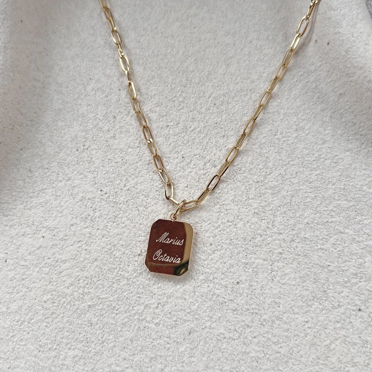 Collier "Ma vérité" avec pendentif rectangulaire personnalisable en acier doré, présenté sur un fond beige texturé.