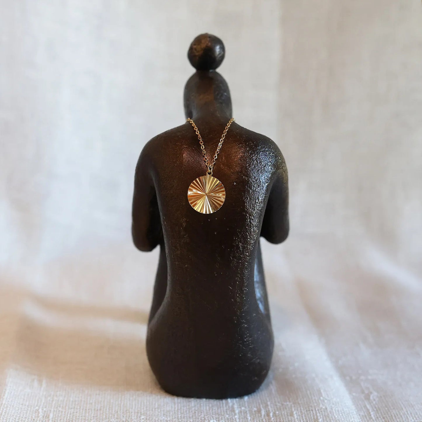 Vue arrière du collier "Energie", pendentif rond strié personnalisable en acier doré, posé sur une statue de femme de dos.
