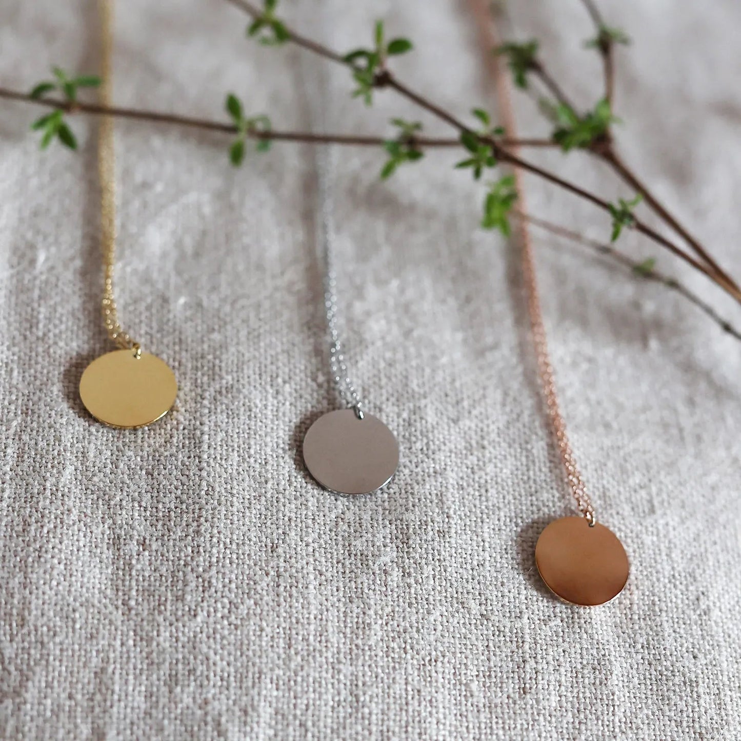 Collier "Reflet" avec médaille ronde personnalisé en acier inoxydable, posé sur un tissu beige texturé.