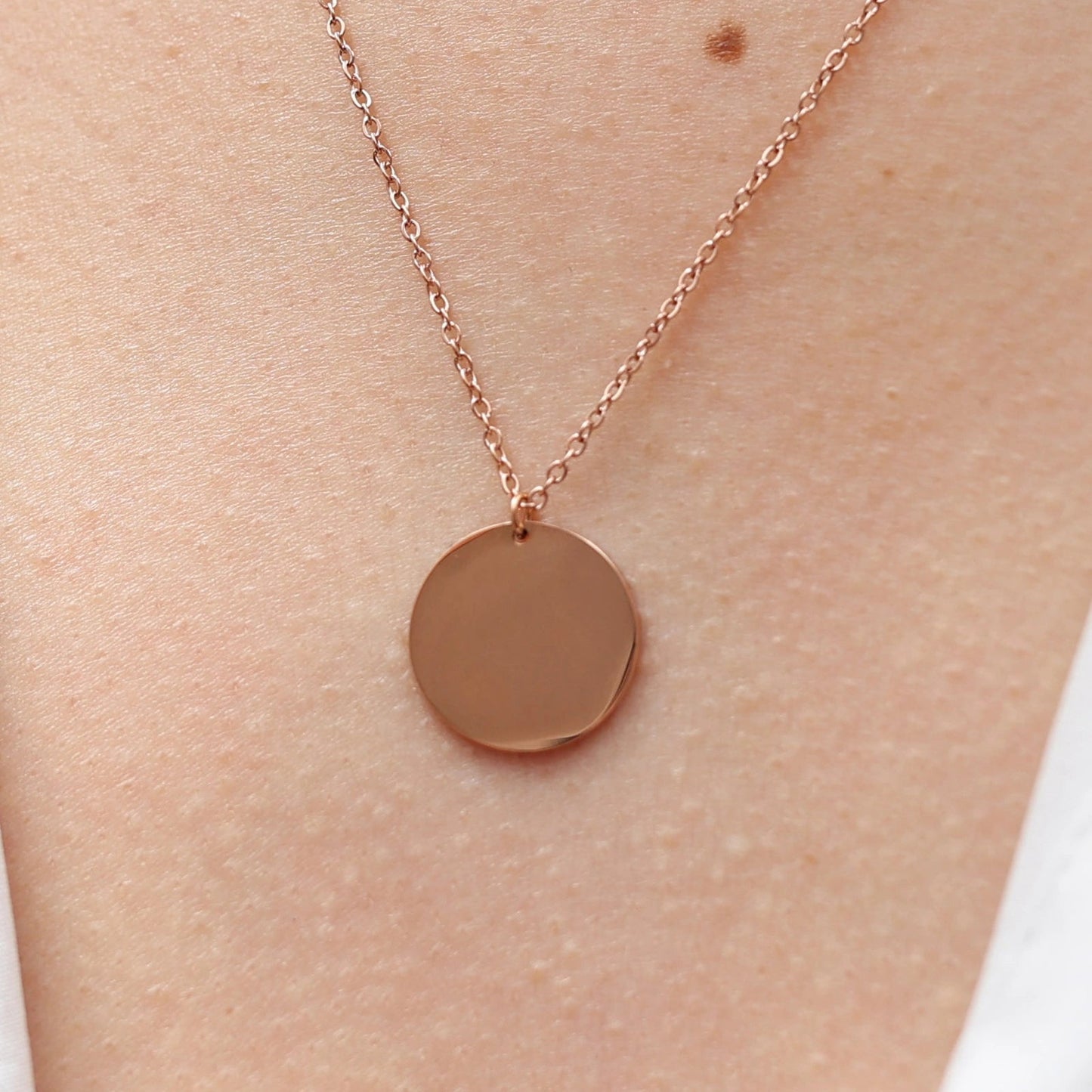 Collier "Reflet" avec médaille ronde personnalisé en acier inoxydable rosé, porté autour du cou.