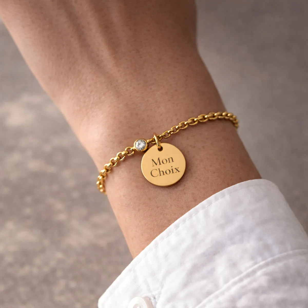 Bracelet Mon choix doré, bijou personnalisable en acier inoxydable avec médaillon gravé "Mon choix" et couleur de naissance blanche, porté au poignet.