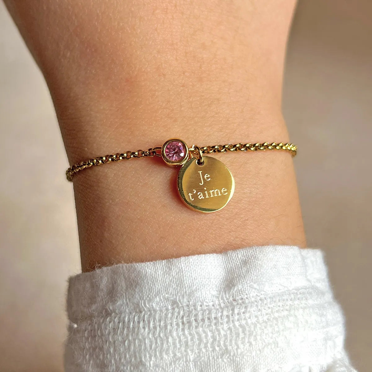 Bracelet Mon choix doré, bijou personnalisable en acier inoxydable avec médaillon gravé "je t'aime" et couleur de naissance rose, porté au poignet.