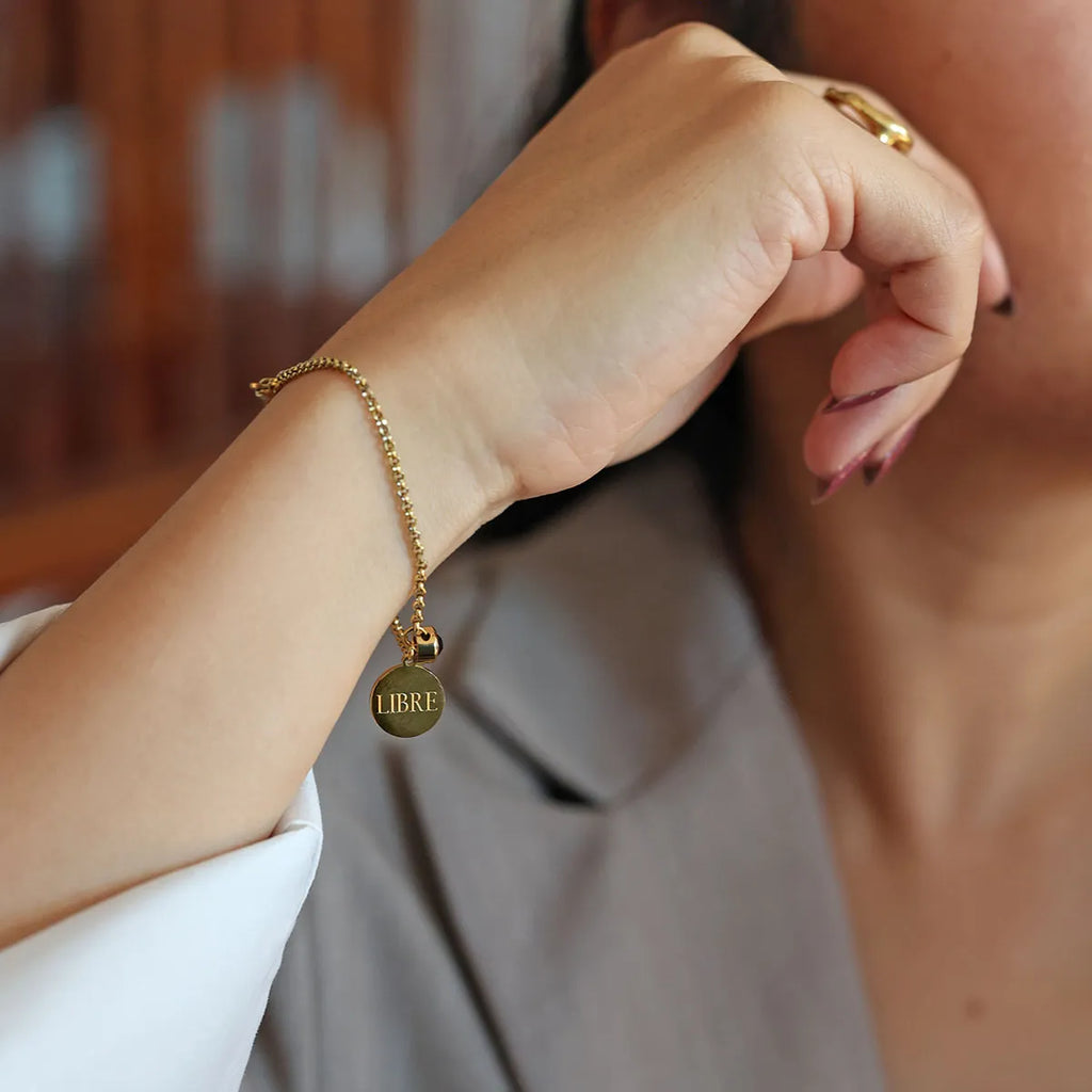 Bracelet Mon choix doré, bijou personnalisable en acier inoxydable avec médaillon gravé "LIBRE" et pierre de naissance violette, porté au poignet.